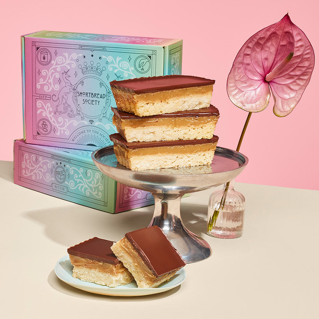 	Millionaire’s Shortbread bars on a silver stand, with Shortbread Society gift boxes and two bars on a plate